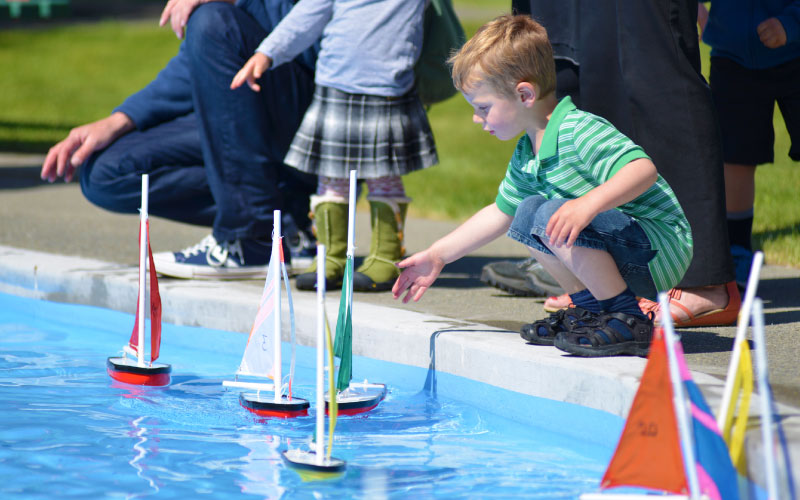 Young child playing with sailing boat toys in pool. 